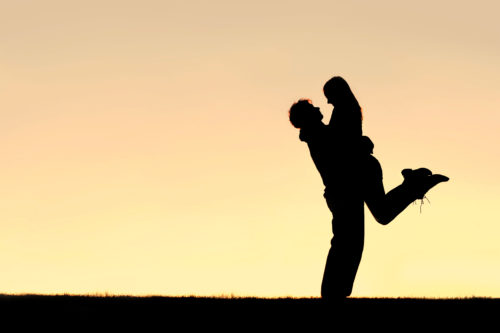 Silhouette of Happy Young Couple Hugging Outside at Sunset A silhouette of a happy young couple hugging, with the man lifting the woman off of her feet, at sunset. Sky leaves room for copy-space.